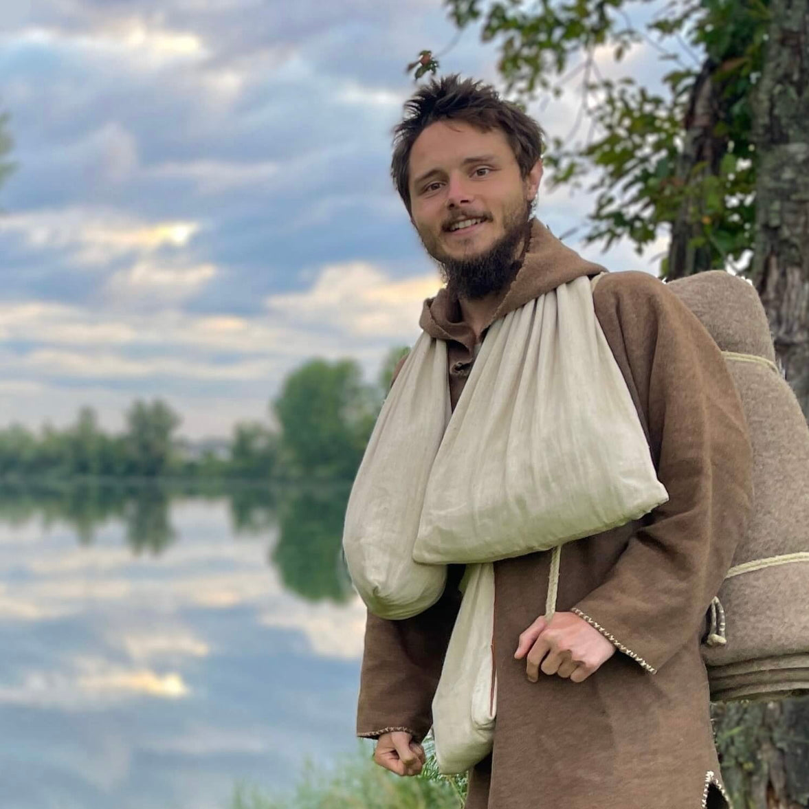 Adrean, der Autor, mit seiner Ausrüstung, Decke und Beuteln, vor einem blauem See, im Grünen, mit blauem Himmel.